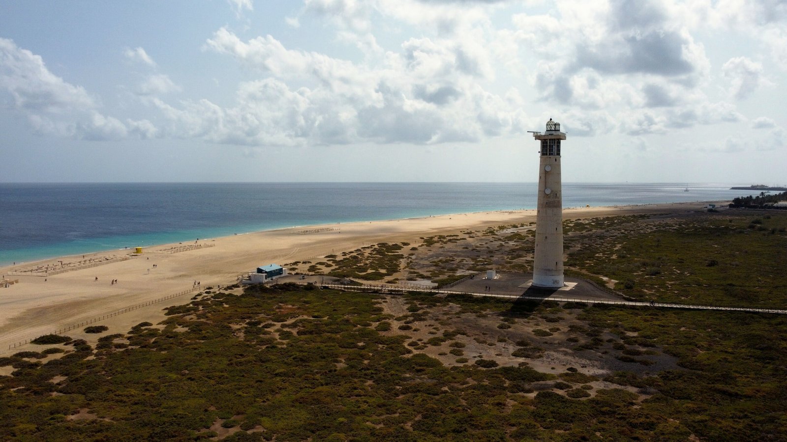 Dronebeeld van een vuurtoren aan de kustlijn, omringd door zand en zee, gefotografeerd vanuit de lucht